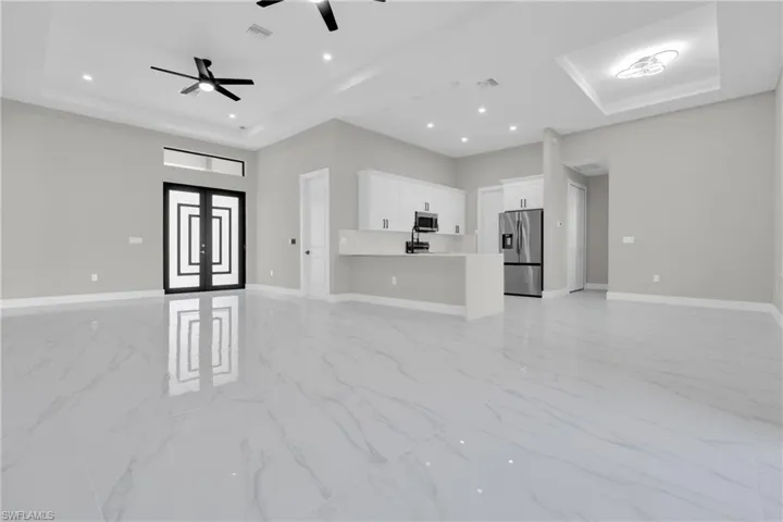 Unfurnished living room with a raised ceiling, light marble finish floors, french doors, recessed lighting, and a ceiling fan