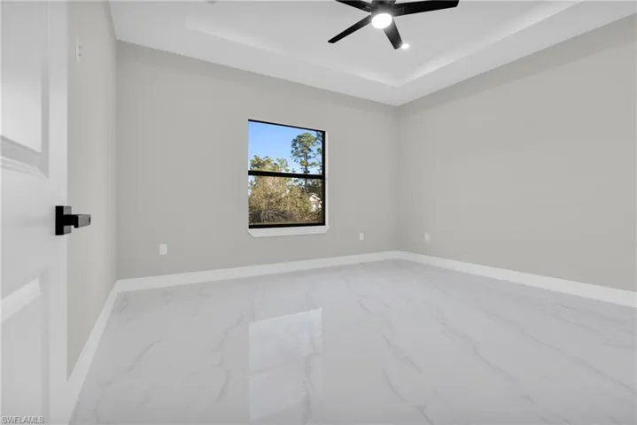 Unfurnished room with marble finish flooring, a tray ceiling, and a ceiling fan