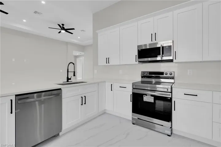 Kitchen with stainless steel appliances, light marble finish floors, white cabinets, recessed lighting, and light stone counters