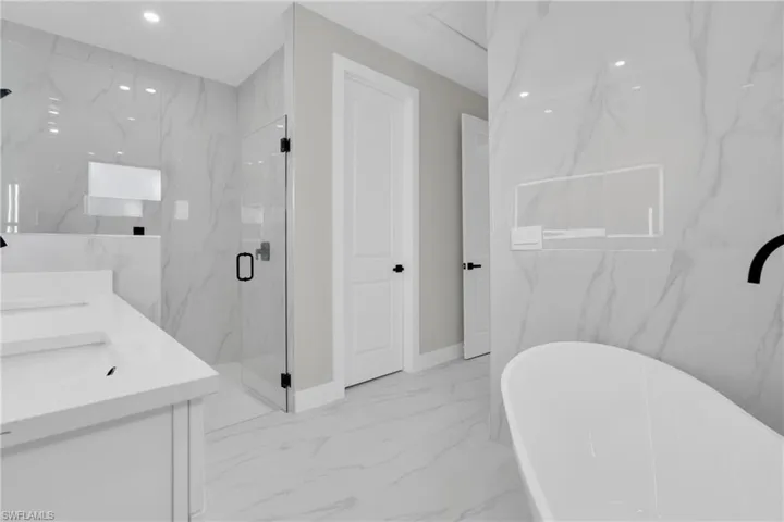 Full bath featuring a soaking tub, double vanity, a marble finish shower, light marble finish floors, and stone wall