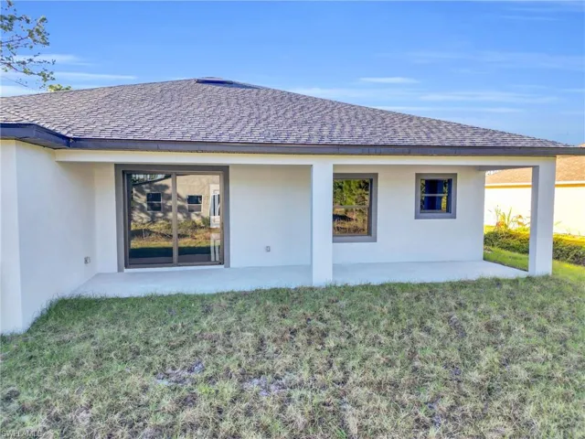 Rear view of house with stucco siding, a yard, roof with shingles, and a patio