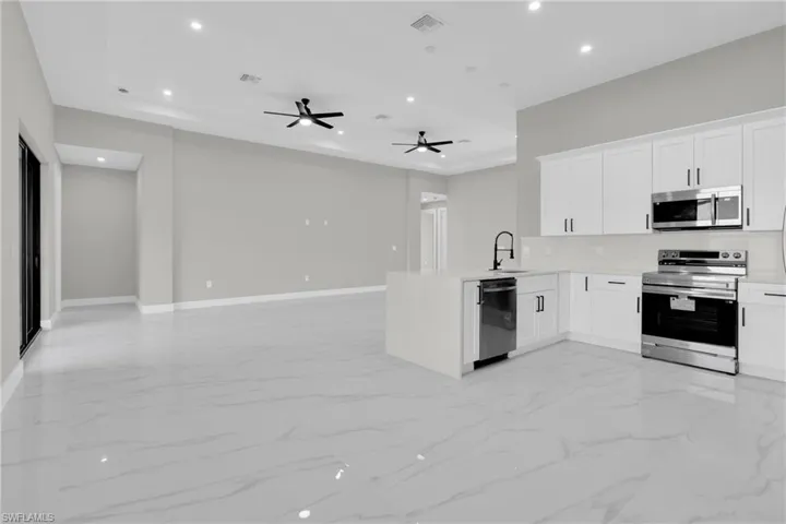 Kitchen with recessed lighting, stainless steel appliances, white cabinetry, and open floor plan