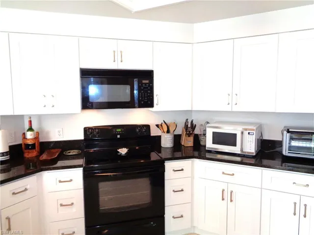 Kitchen featuring black appliances, white cabinetry, and dark stone counters
