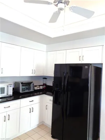 Kitchen with black fridge with ice dispenser, white cabinets, white microwave, dark countertops, and light tile patterned floors