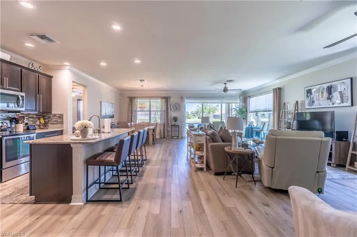 Kitchen featuring a center island with sink, appliances with stainless steel finishes, a kitchen breakfast bar, light wood-type flooring, and dark brown cabinetry