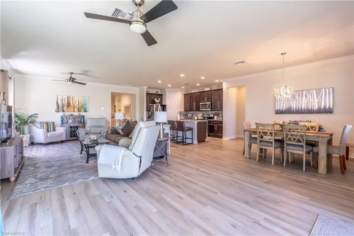Living room with crown molding, light wood-type flooring, and ceiling fan with notable chandelier