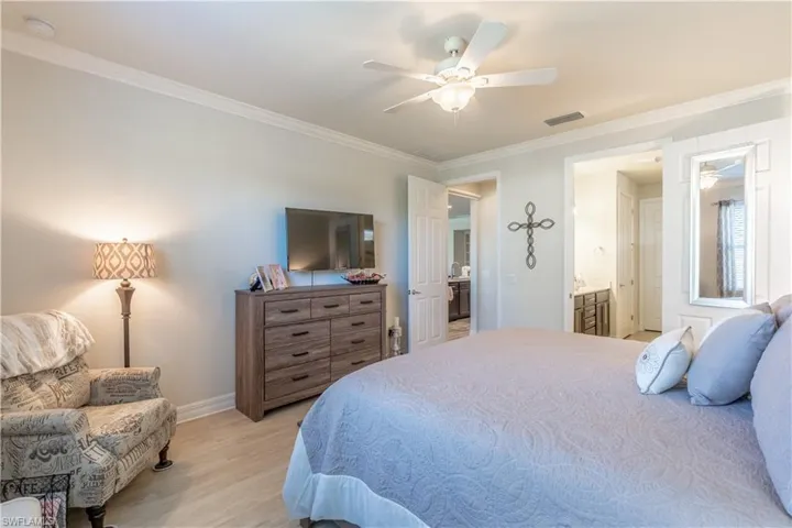 Bedroom featuring light hardwood / wood-style floors, ornamental molding, ensuite bathroom, and ceiling fan
