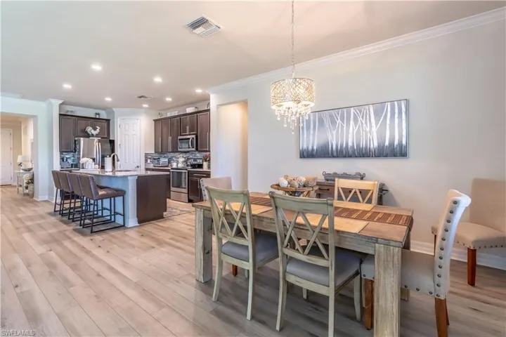 Dining space with a notable chandelier, light hardwood / wood-style floors, crown molding, and sink