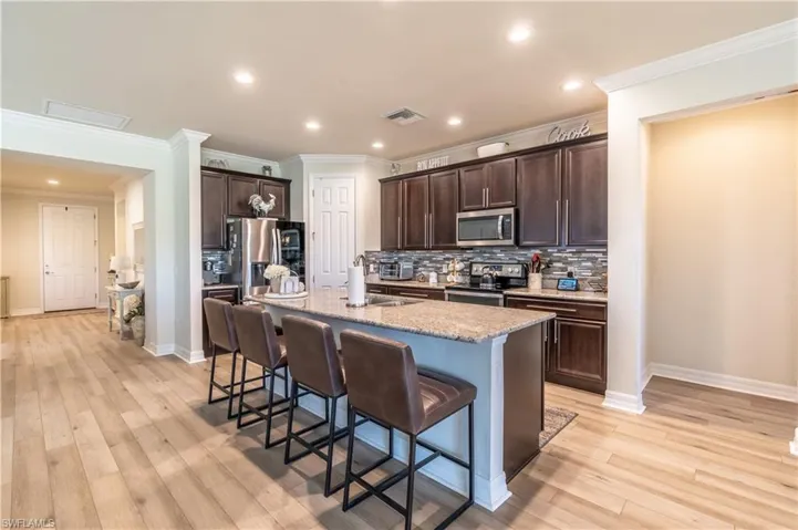 Kitchen with decorative backsplash, appliances with stainless steel finishes, a kitchen island with sink, and light hardwood / wood-style floors