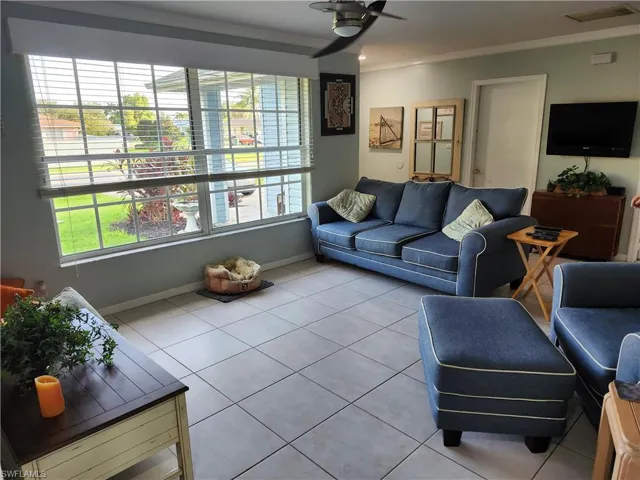 Living room with ceiling fan, light tile patterned flooring, and ornamental molding
