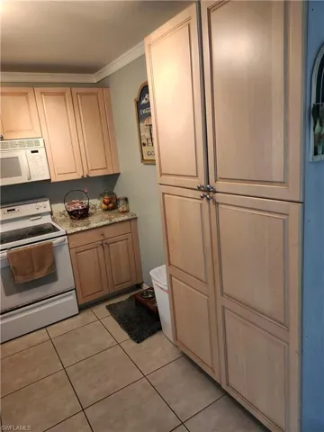 Kitchen featuring light tile patterned flooring, white appliances, crown molding, and light brown cabinetry