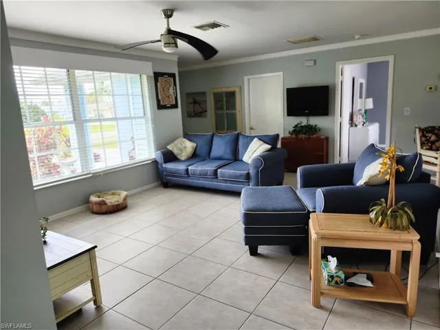 Living room with ceiling fan, crown molding, and light tile patterned floors