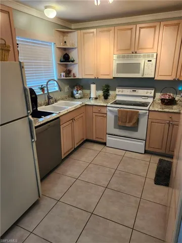 Kitchen featuring white appliances, light tile patterned floors, sink, ornamental molding, and light brown cabinets