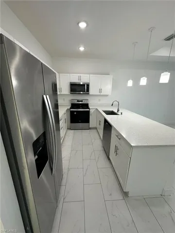 Kitchen featuring stainless steel appliances, light marble finish flooring, a peninsula, white cabinets, and light stone countertops
