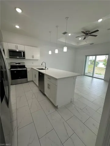 Kitchen featuring light marble finish flooring, a peninsula, stainless steel appliances, decorative light fixtures, and a raised ceiling