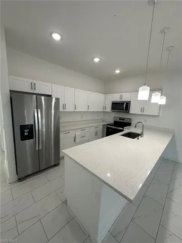 Kitchen featuring light marble finish floors, a peninsula, stainless steel appliances, and white cabinets