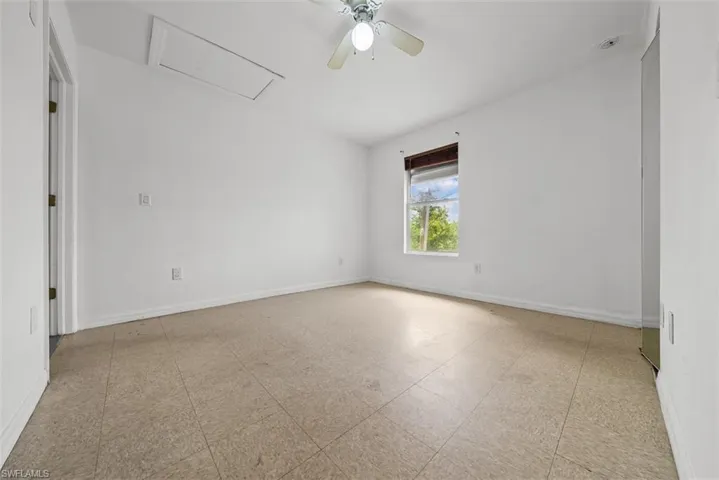 Room featuring neutral wall tones, square tile flooring, a window with exterior greenery, and a ceiling fan with integrated lighting