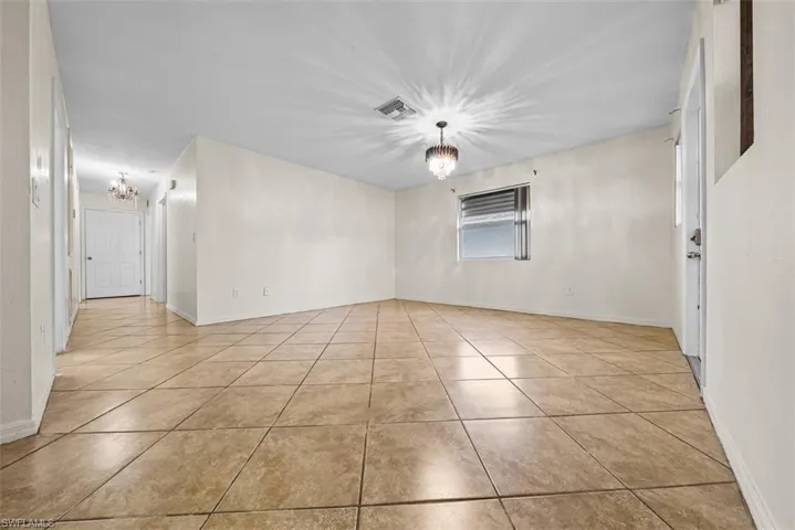 Spacious room featuring neutral-toned tile flooring, white walls, and a window with blinds