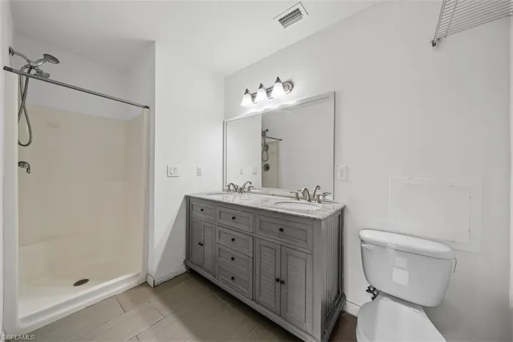 Bathroom featuring a dual-sink vanity with a light gray wood-finish cabinet, a large framed mirror, and a walk-in shower with a shower head and handheld sprayer