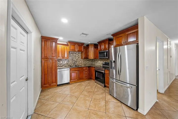 Kitchen featuring wood cabinetry, stainless steel appliances, mosaic tile backsplash, and tile flooring