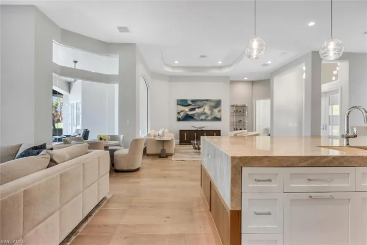 Kitchen featuring open floor plan, pendant lighting, light wood-style flooring, white cabinetry, and a tray ceiling
