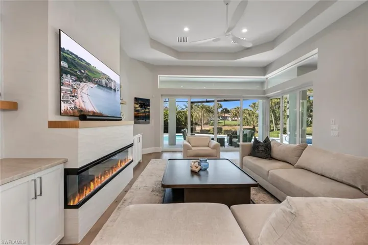Living room featuring a tiled fireplace, light wood-type flooring, a ceiling fan, recessed lighting, and a high tray ceiling