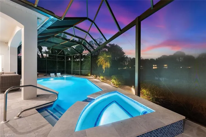 Pool at dusk featuring a patio, a sunroom, glass enclosure, and a pool with connected hot tub