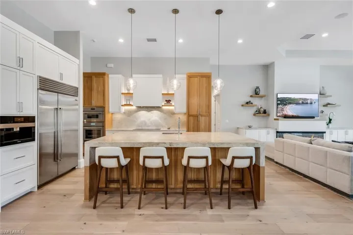 Dual tone kitchen featuring open floor plan, open shelves, light wood-type flooring, a center island with sink, and dual tone cabinets