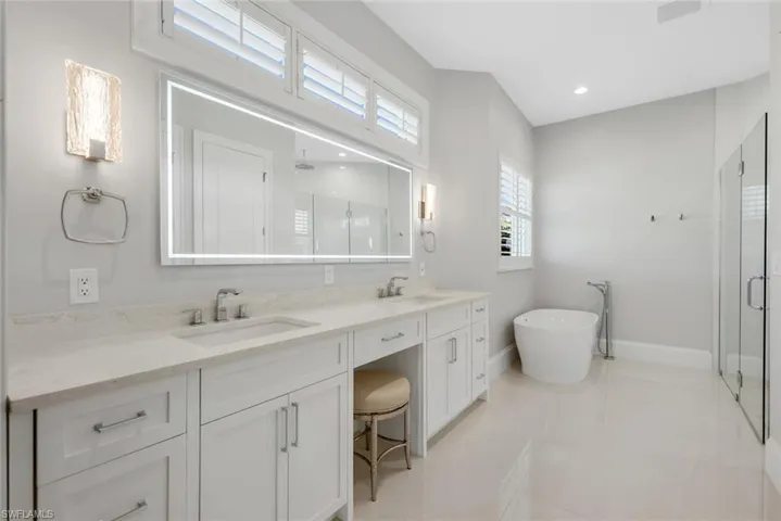 Full bath featuring double vanity, a shower stall, a freestanding bath, recessed lighting, and light tile patterned floors