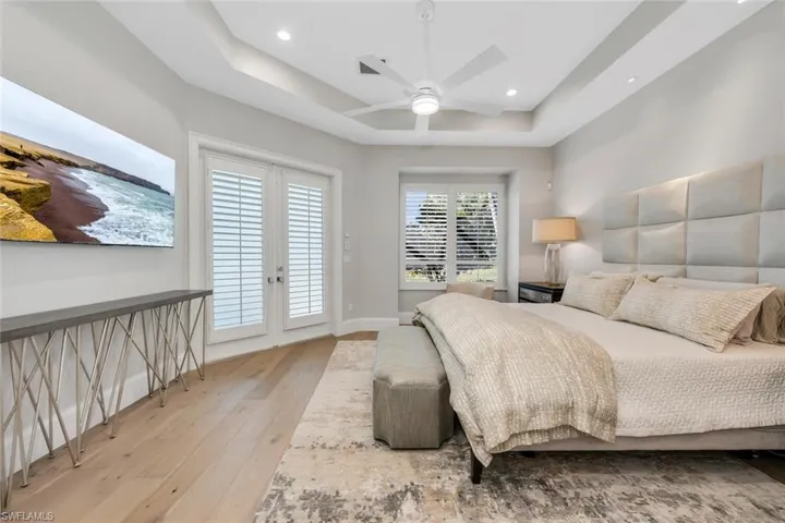 Bedroom with french doors, access to outside, a tray ceiling, light wood-style flooring, and ceiling fan