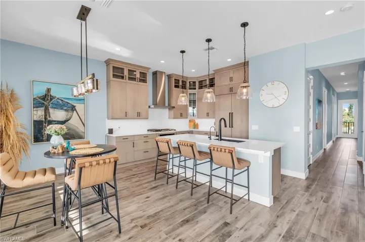 Kitchen with pendant lighting, light brown cabinetry, light hardwood / wood-style flooring, an island with sink, and wall chimney range hood
