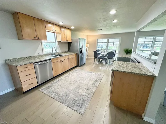 Kitchen with sink, light hardwood / wood-style flooring, stainless steel appliances, and light stone counters