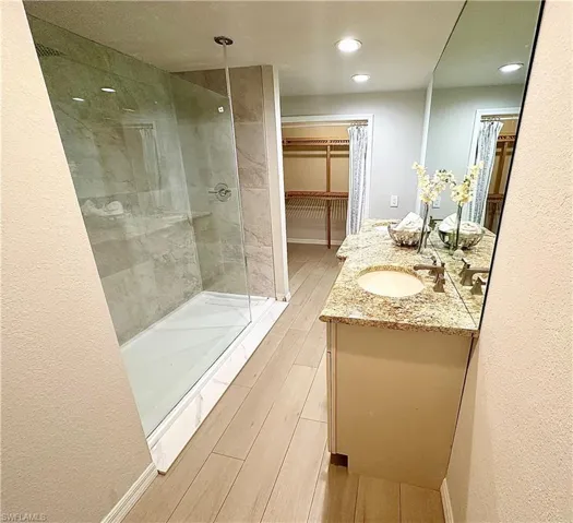 Bathroom with wood-type flooring, a shower with shower door, and vanity