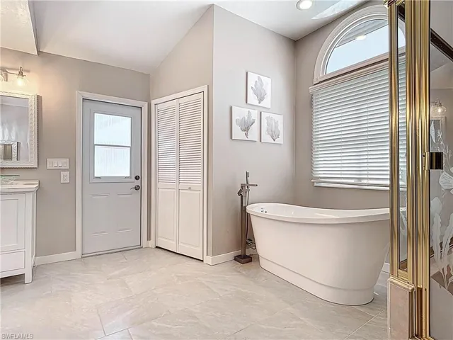 Full bath with plenty of natural light, a freestanding bath, vanity, and a closet
