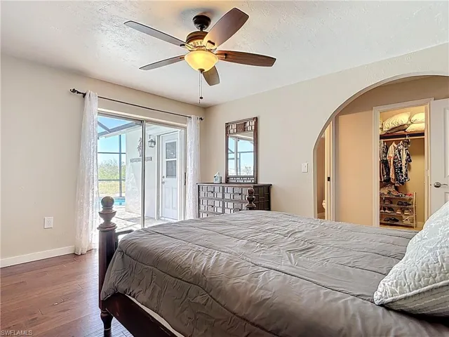 Bedroom featuring multiple windows, a textured ceiling, a walk in closet, wood-type flooring, and access to exterior