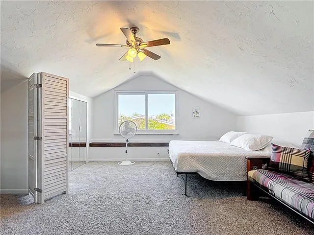 Carpeted bedroom featuring a textured ceiling, lofted ceiling, and ceiling fan