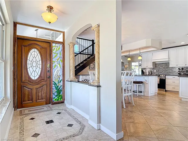 Entrance foyer with inlaid floor details, light tile patterned floors, arched walkways, ornate columns, and stairway