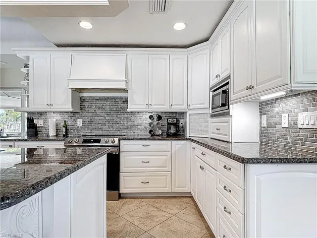 Kitchen with dark stone countertops, white cabinets, appliances with stainless steel finishes, and recessed lighting