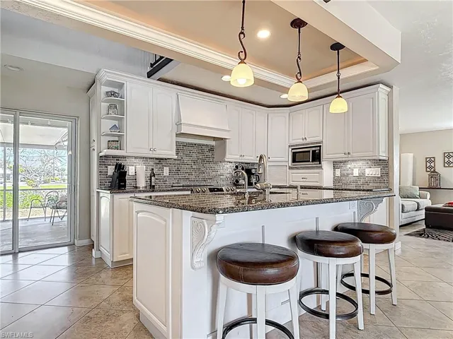 Kitchen with dark stone counters, open shelves, a breakfast bar, white cabinetry, and a center island with sink