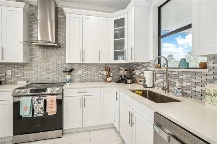 Kitchen featuring stainless steel appliances, decorative backsplash, wall chimney exhaust hood, sink, and light tile patterned flooring