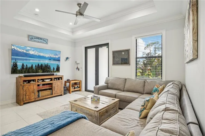 Living room featuring ceiling fan, a raised ceiling, crown molding, and light tile patterned floors