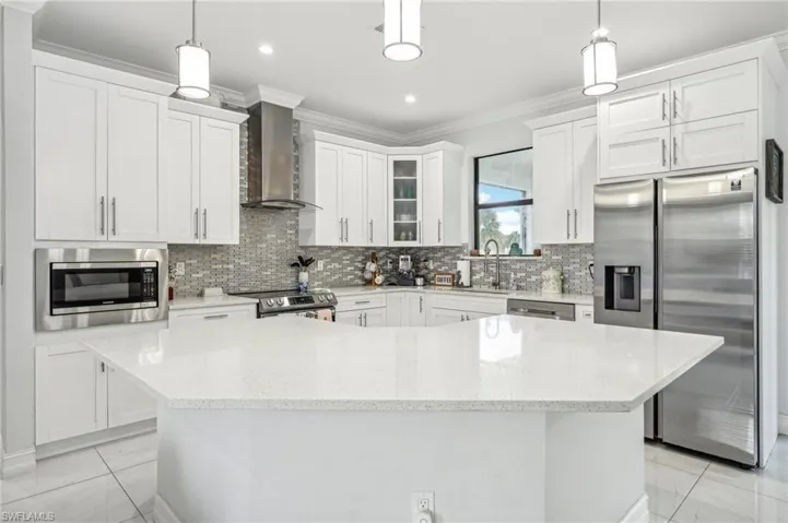 Kitchen with backsplash, stainless steel appliances, wall chimney range hood, and light tile patterned floors