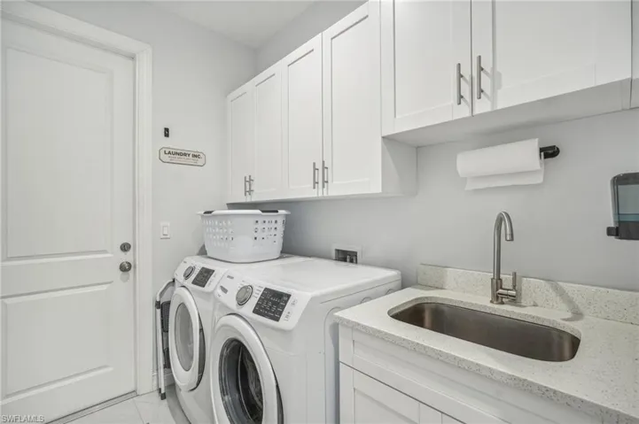 Clothes washing area with sink, cabinets, separate washer and dryer, and light tile patterned floors
