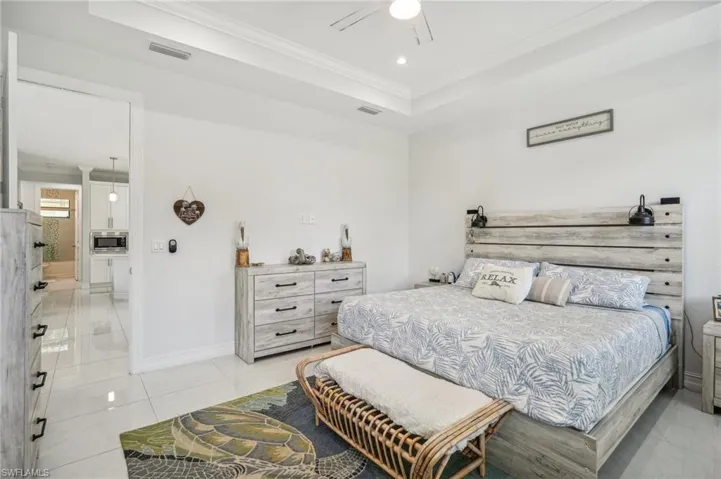 Tiled bedroom featuring ceiling fan, a tray ceiling, and ornamental molding
