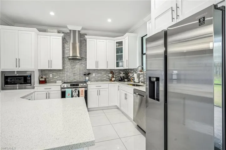 Kitchen featuring appliances with stainless steel finishes, crown molding, wall chimney range hood, and sink