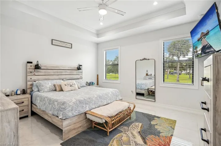 Tiled bedroom with ceiling fan, a raised ceiling, and ornamental molding