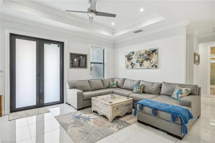 Tiled living room featuring a tray ceiling, ceiling fan, crown molding, and french doors
