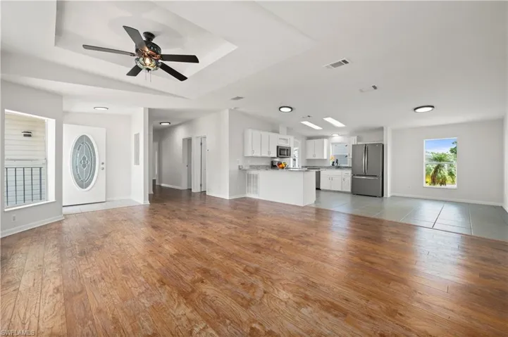 Unfurnished living room featuring light wood-style floors, a raised ceiling, and a ceiling fan