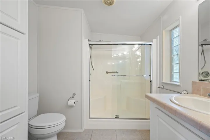 Full bathroom with vanity, a shower stall, light tile patterned flooring, vaulted ceiling, and crown molding