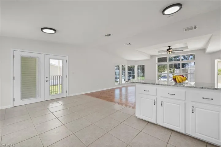 Kitchen with light tile patterned floors, light stone counters, white cabinetry, open floor plan, and a ceiling fan